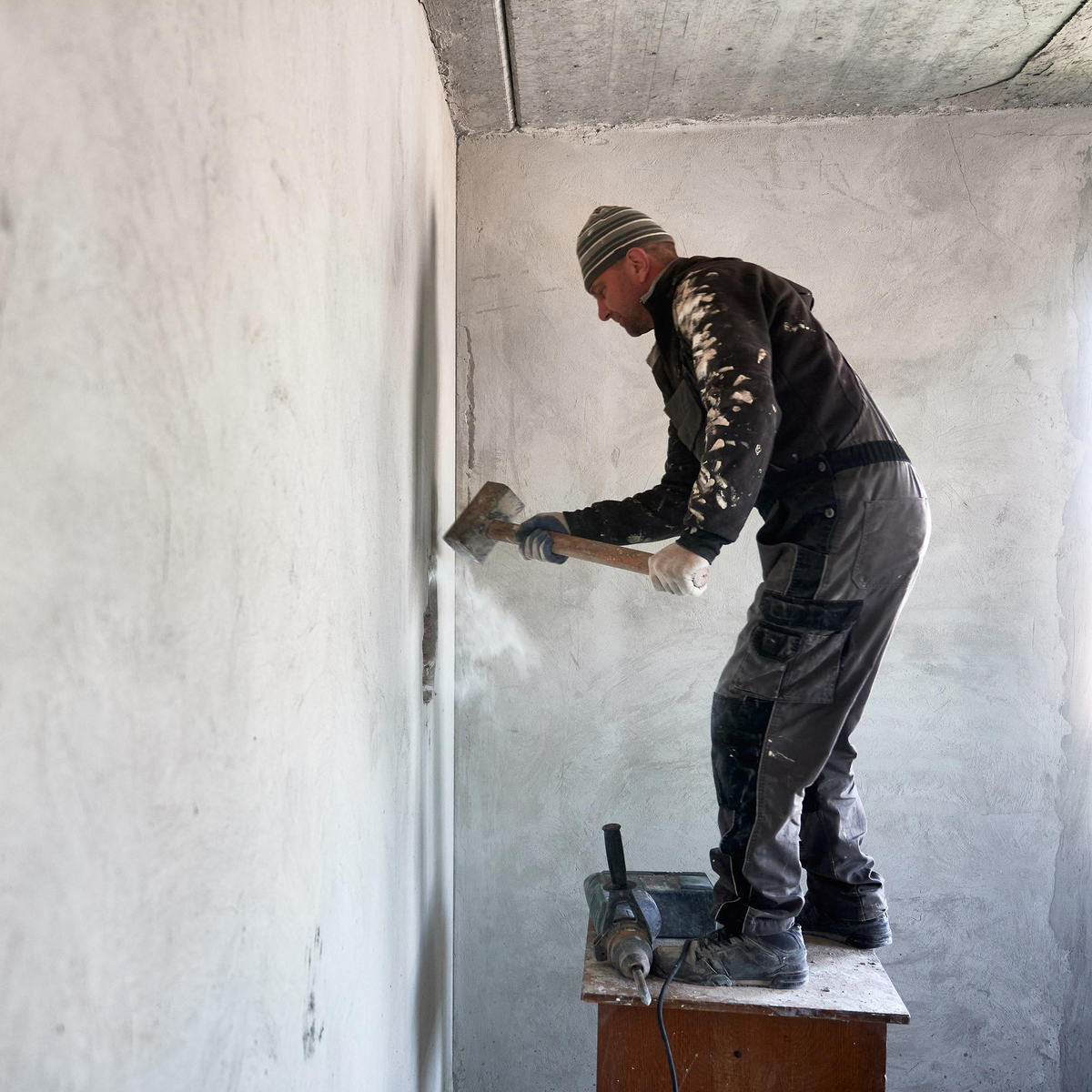Arbeiter schlägt mit Axt auf Betonwand in Rohbau.