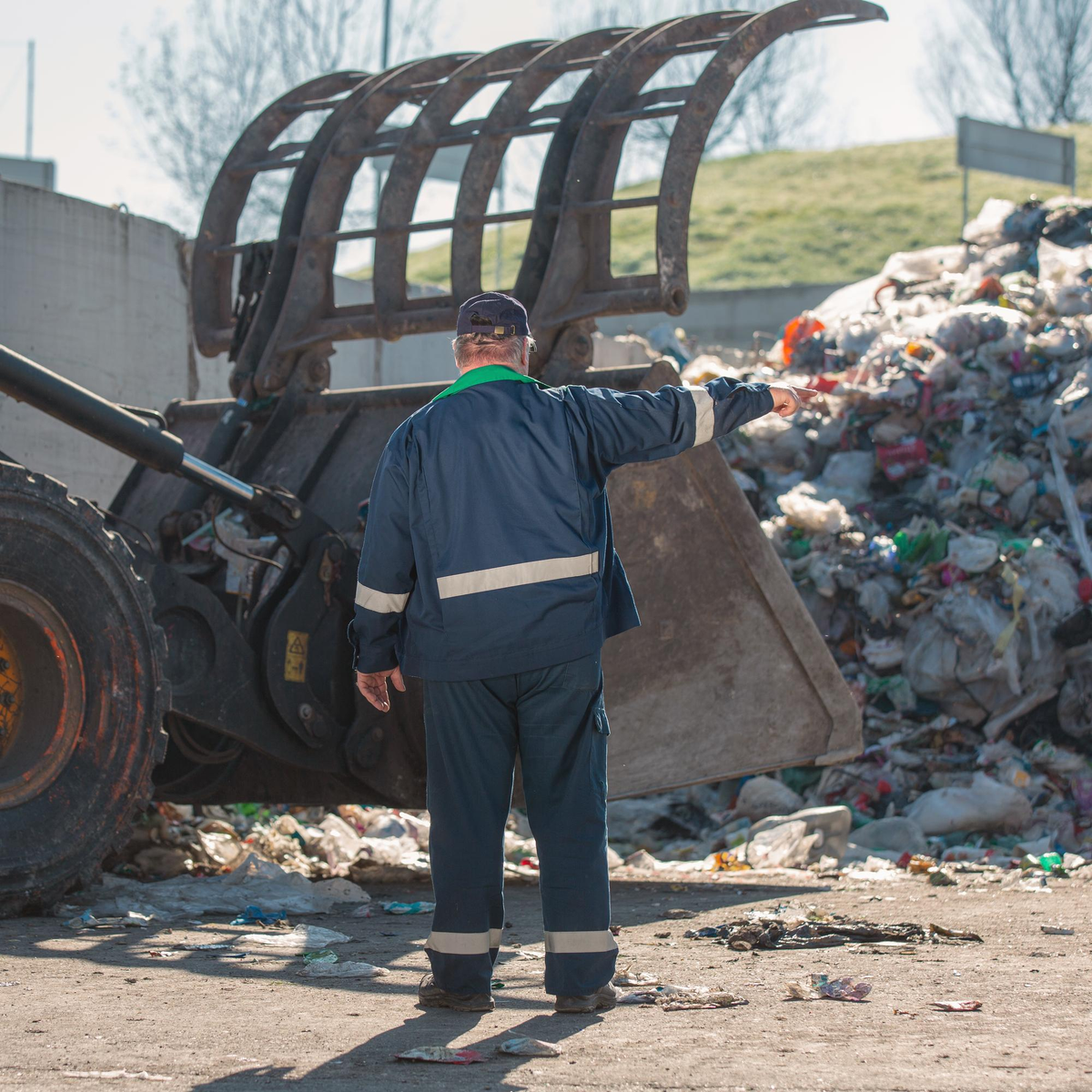 Arbeiter dirigiert Bagger auf einem Müllentsorgungsgelände.