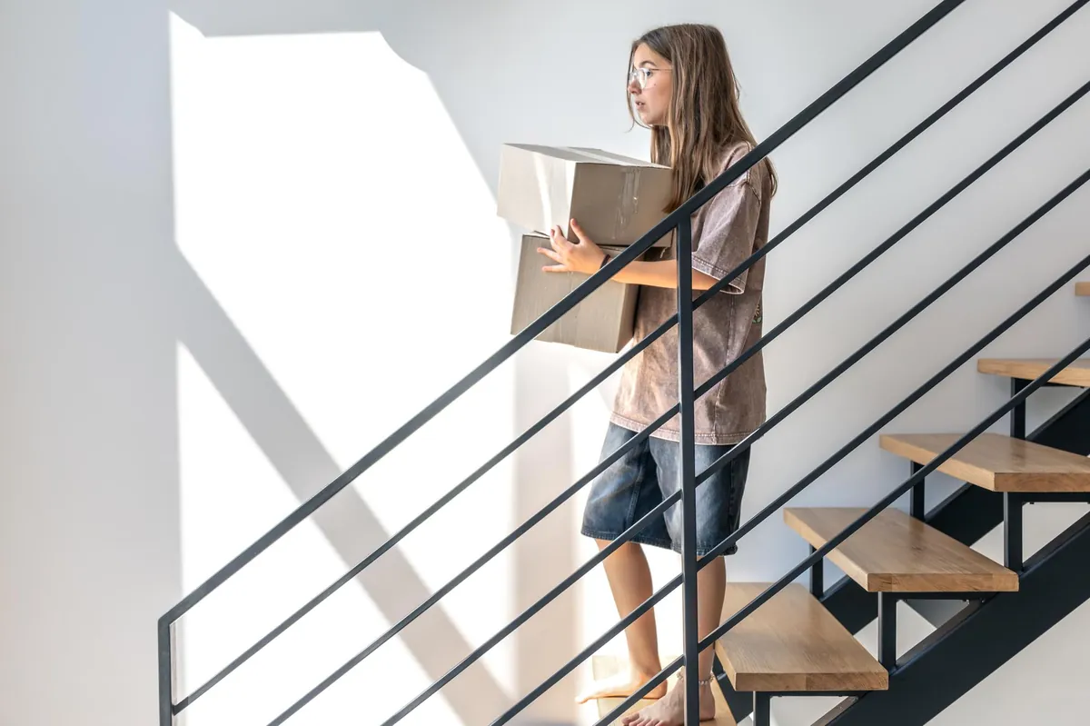 Mädchen mit Brille trägt Karton eine Treppe hinauf.