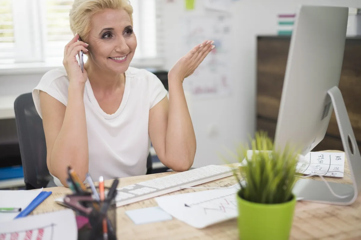Blonde Frau telefoniert lächelnd am Schreibtisch im Büro.