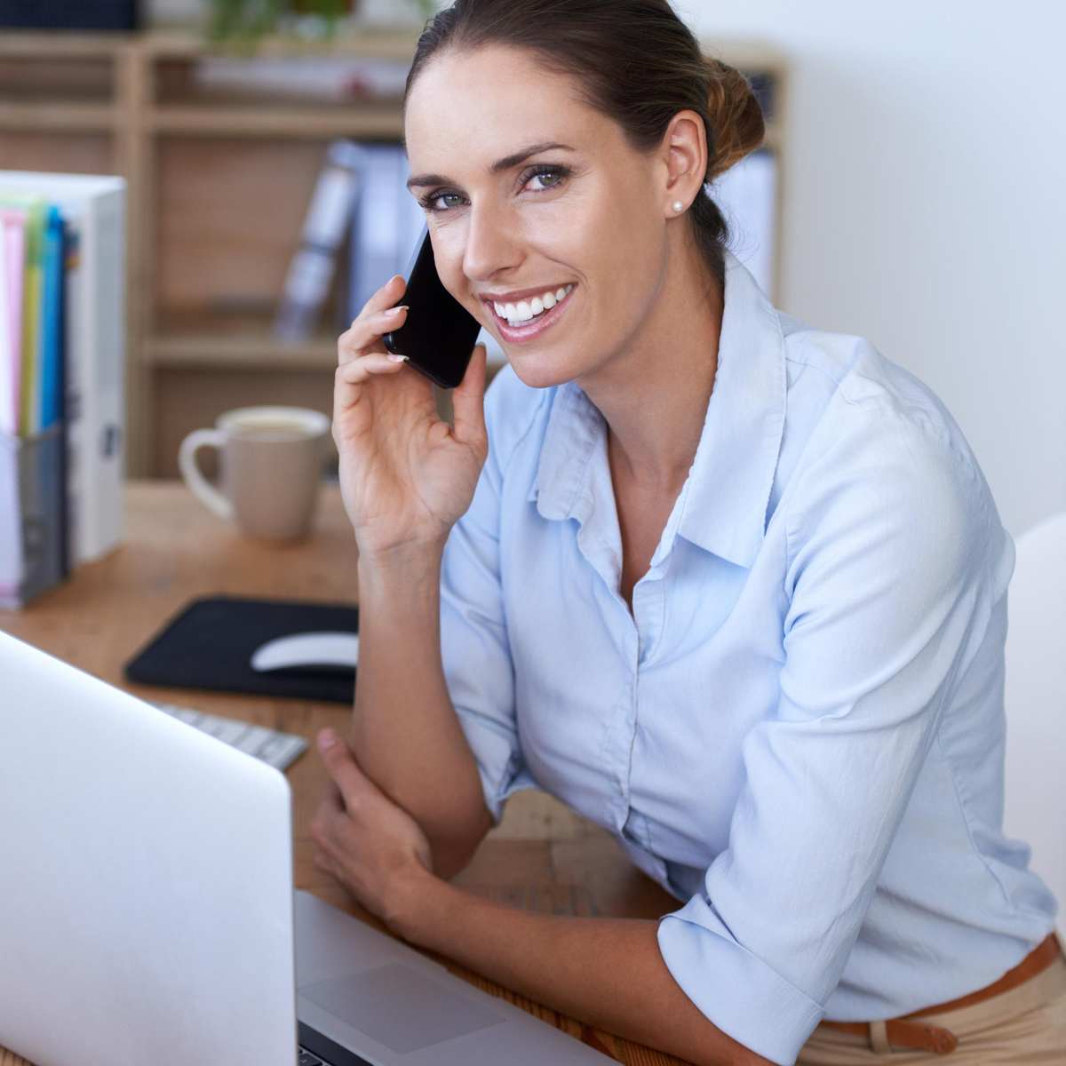Lächelnde Frau telefoniert am Schreibtisch mit Laptop.