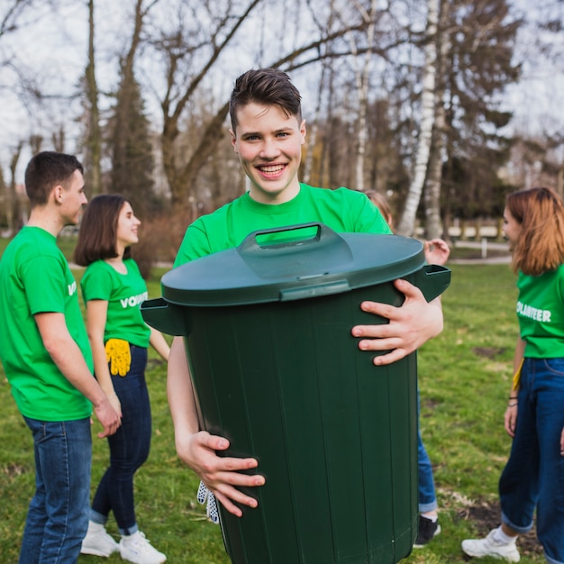 Lächelnder Freiwilliger hält grüne Mülltonne im Park.