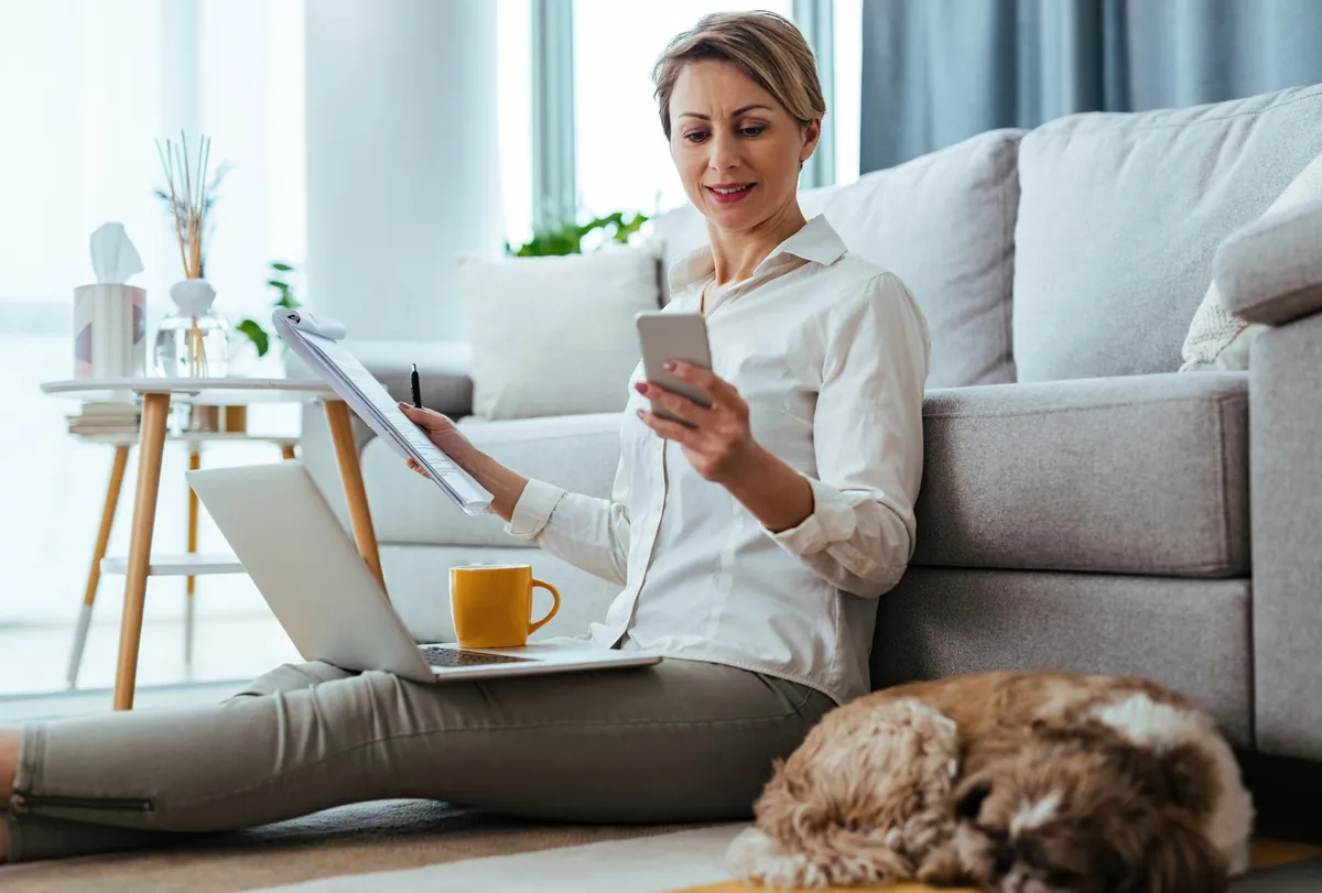 Frau arbeitet zu Hause mit Laptop, Smartphone und Hund.