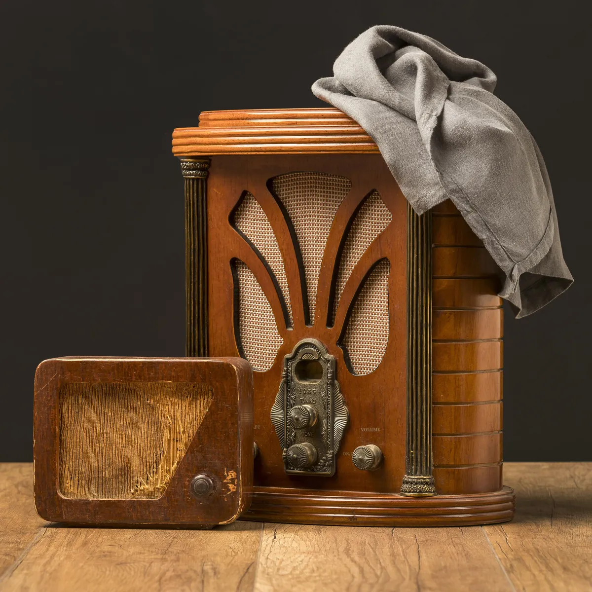 Zwei antike Holzradios mit grauem Tuch auf Holztisch.