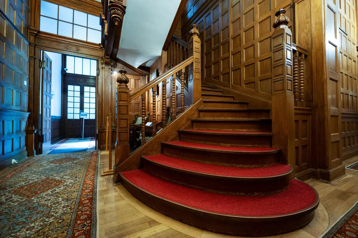 Prunkvolle Holztreppe mit rotem Teppich in historischem Herrenhaus.