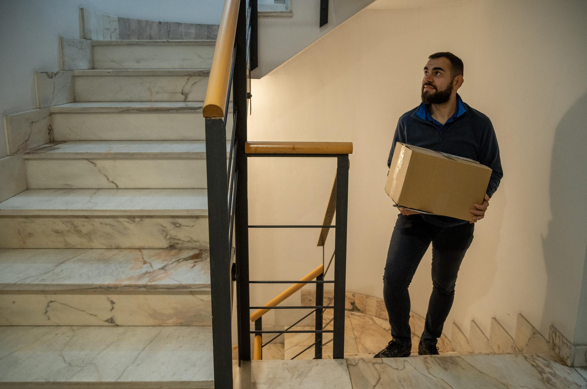 Mann trägt Karton eine Marmortreppe hinauf.
