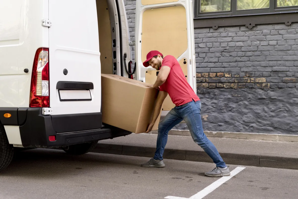 Liefermann entlädt schweren Karton aus weißem Transporter.