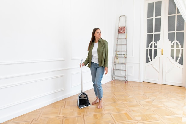 Frau mit Kehrschaufel reinigt helles, leeres Zimmer.
