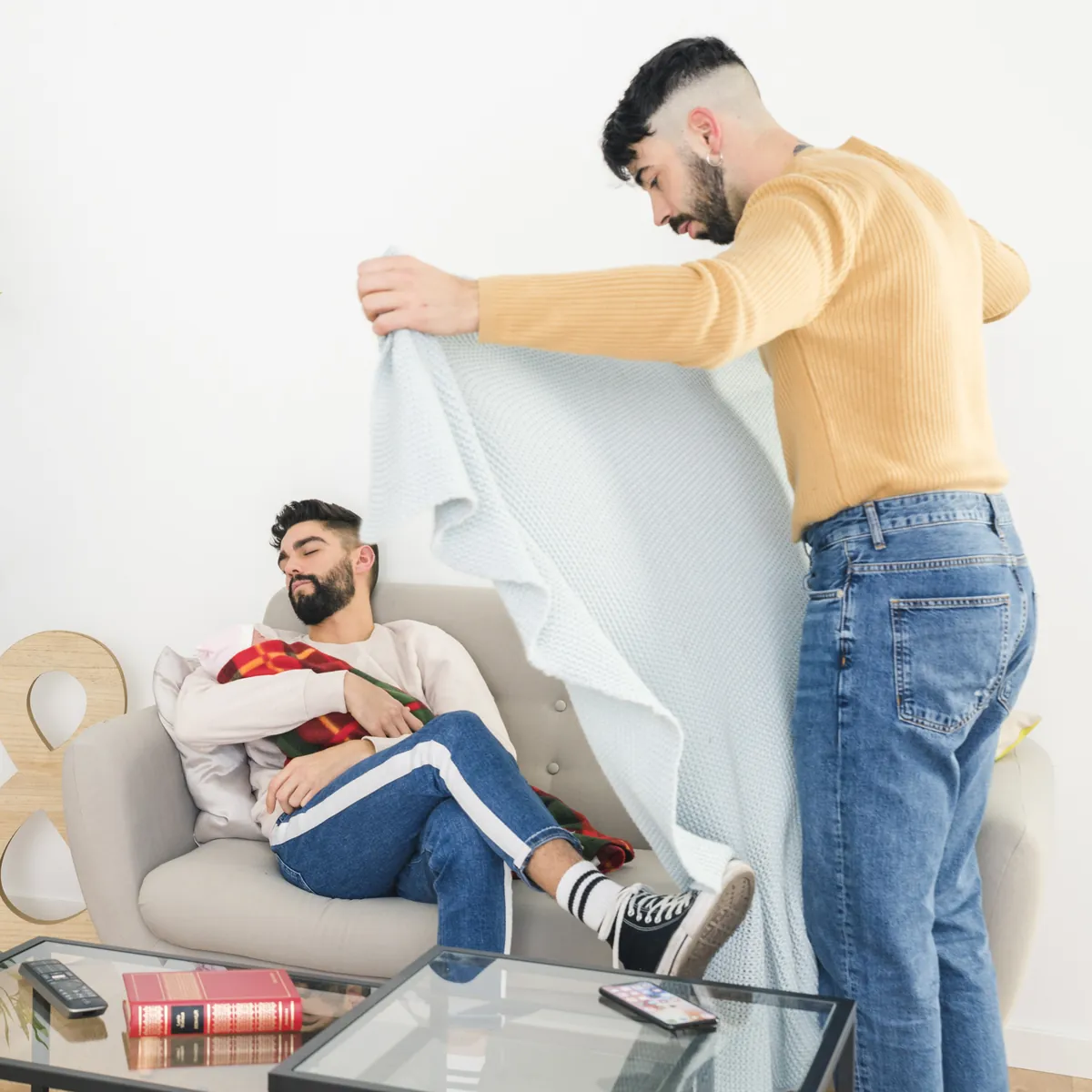 Ein Mann deckt einen schlafenden Mann auf dem Sofa zu.