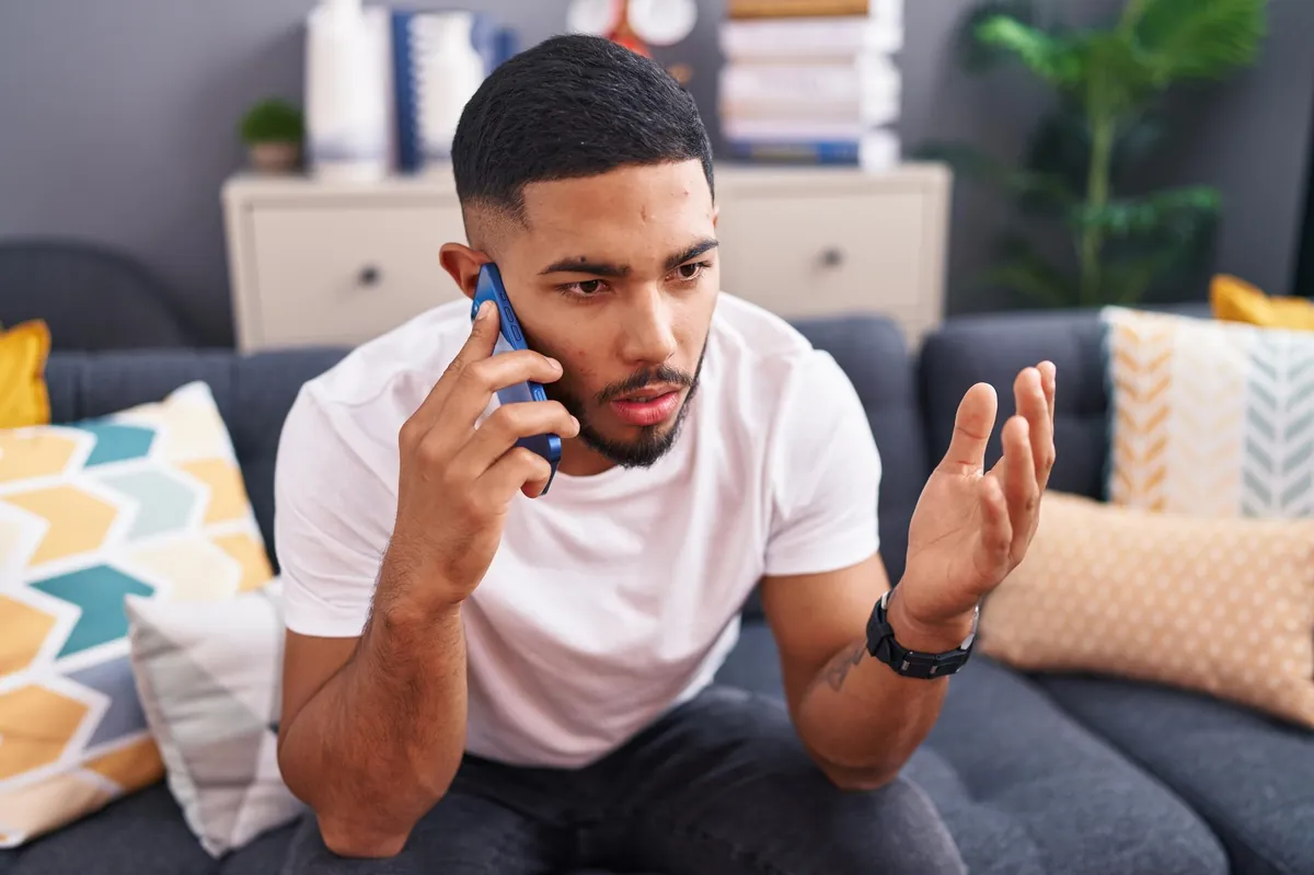 Ein junger Mann telefoniert frustriert auf dem Sofa.
