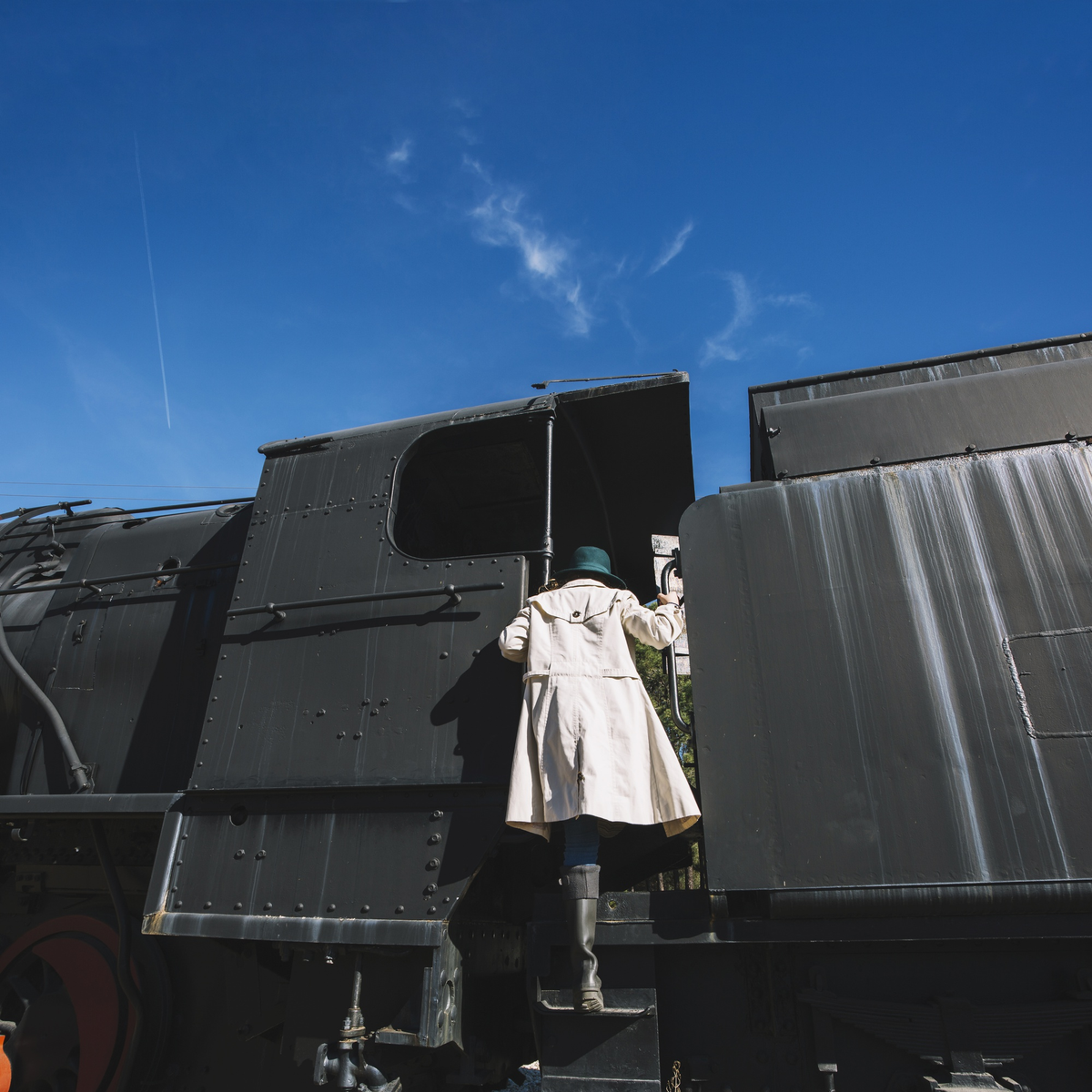 Person in weißem Mantel besteigt schwarze Dampflokomotive.