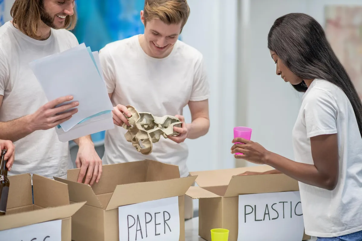 Drei junge Menschen sortieren Müll in Recyclingboxen.