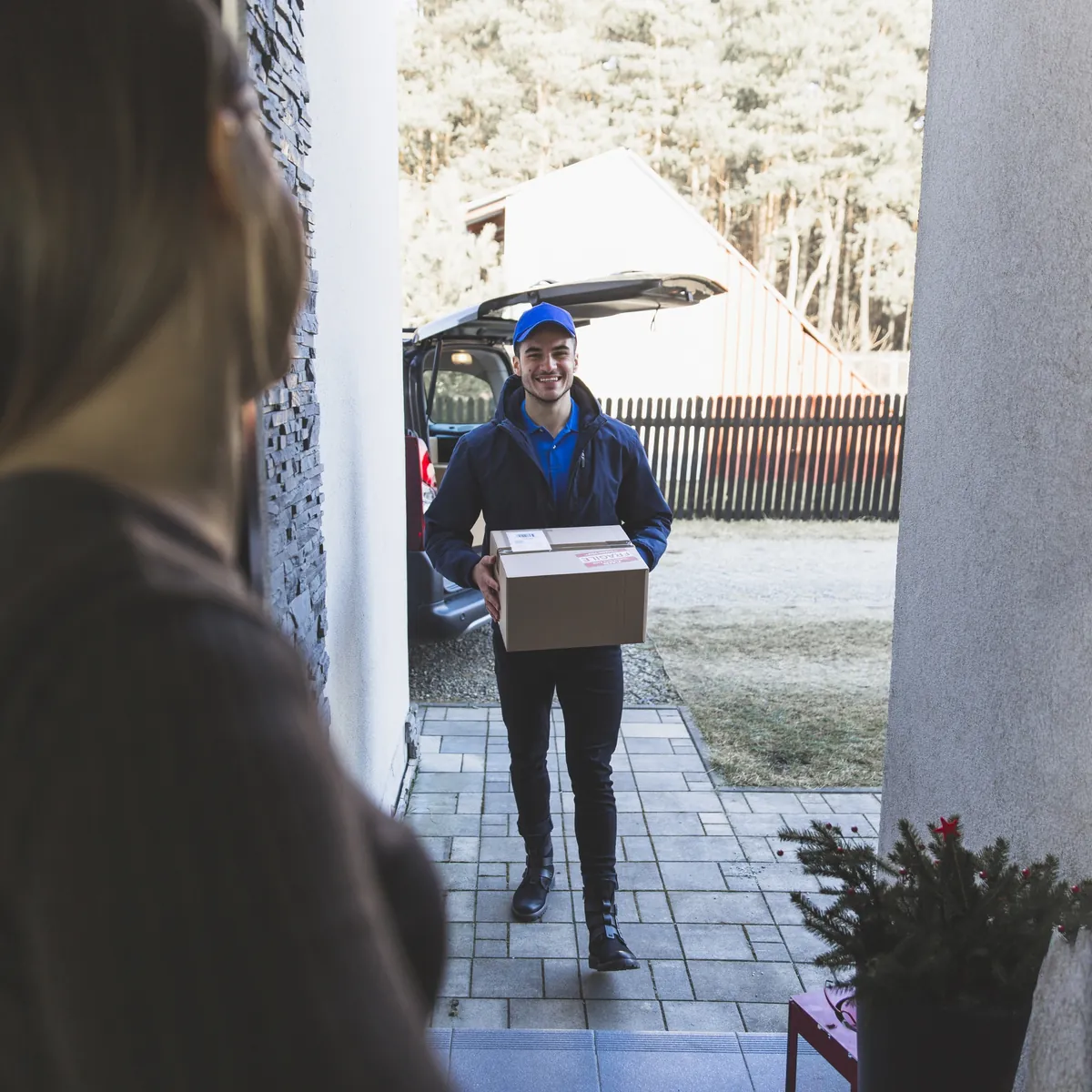 Lächelnder Paketbote liefert Karton an Haustür.