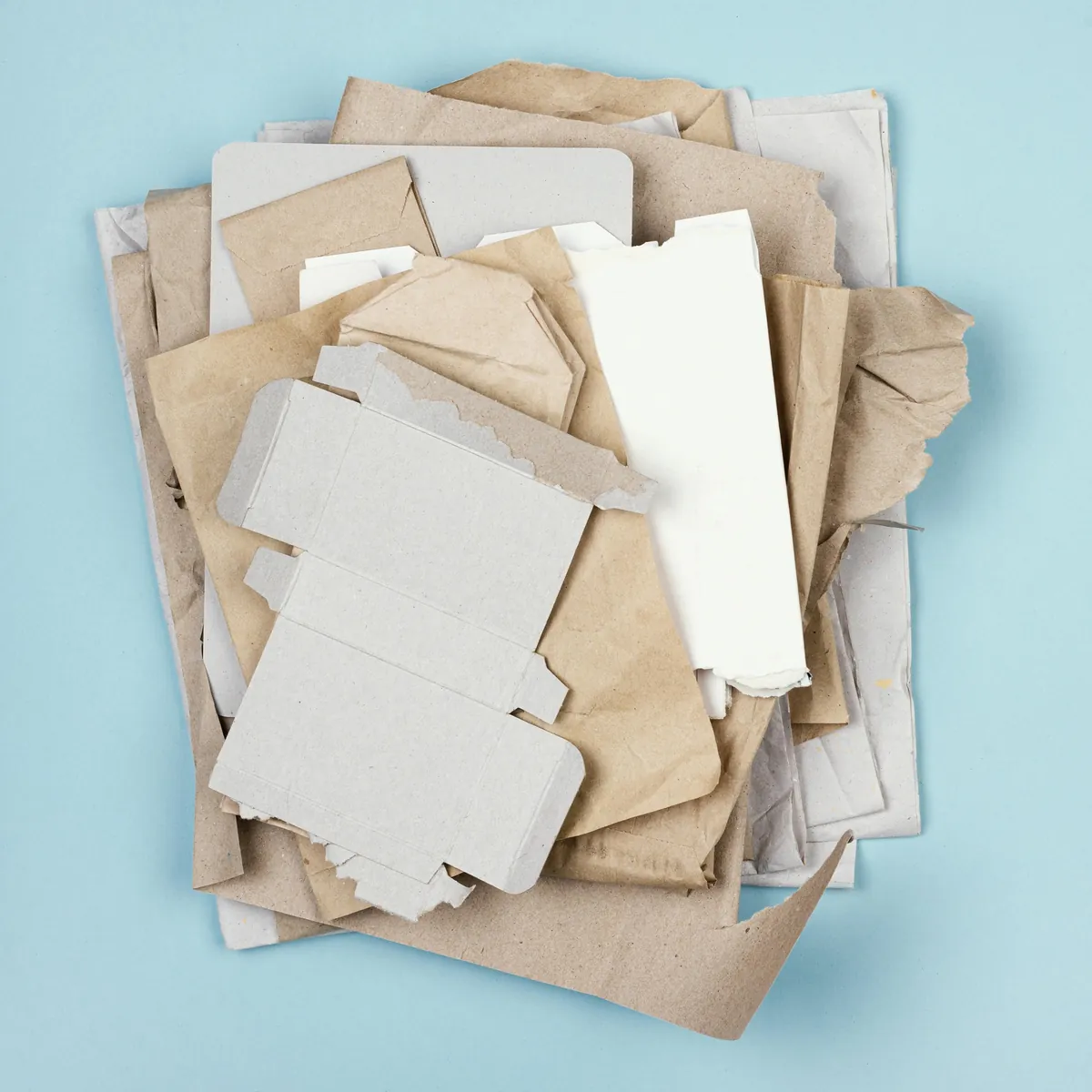 Stapel aus verschiedenen Papier- und Kartonabfällen auf blauem Hintergrund.