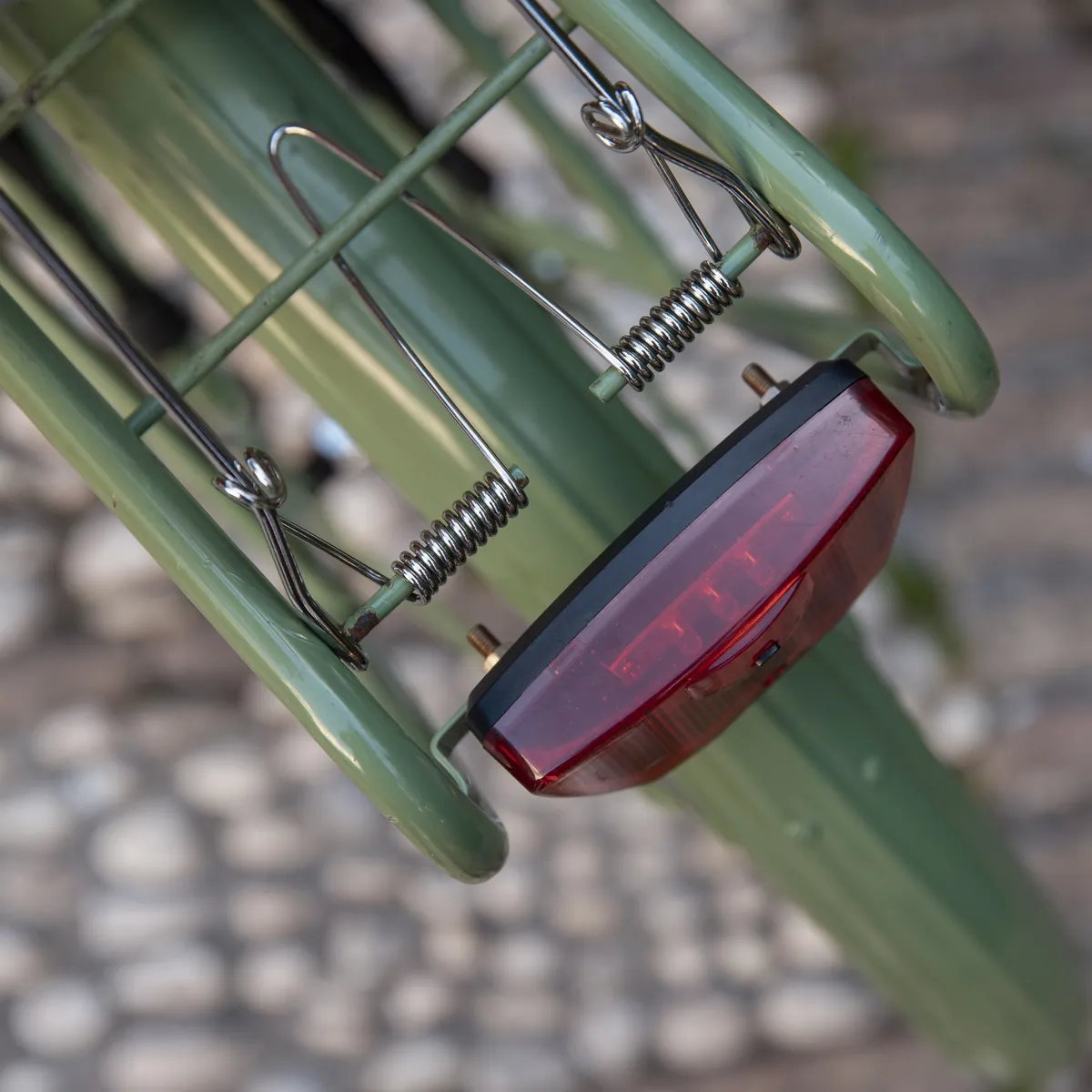 Rotes Rücklicht an grünem Fahrradgepäckträger mit Federn.