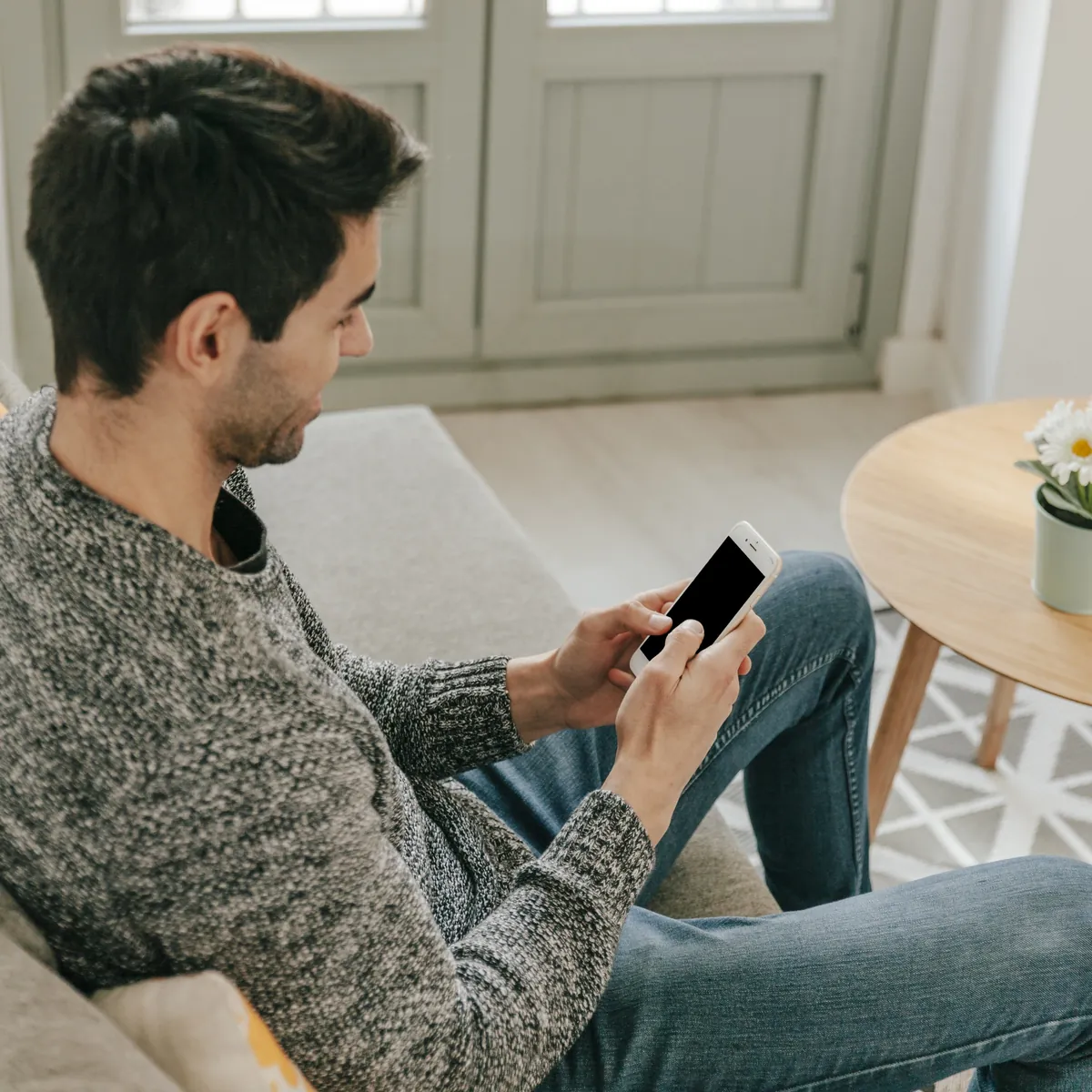 Mann sitzt auf Sofa und schaut auf Smartphone.