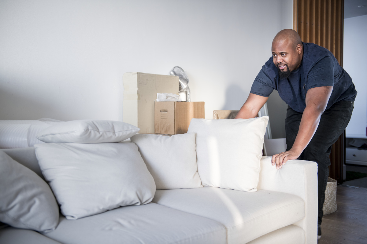 Mann schiebt weißes Sofa in ein neues Zuhause.