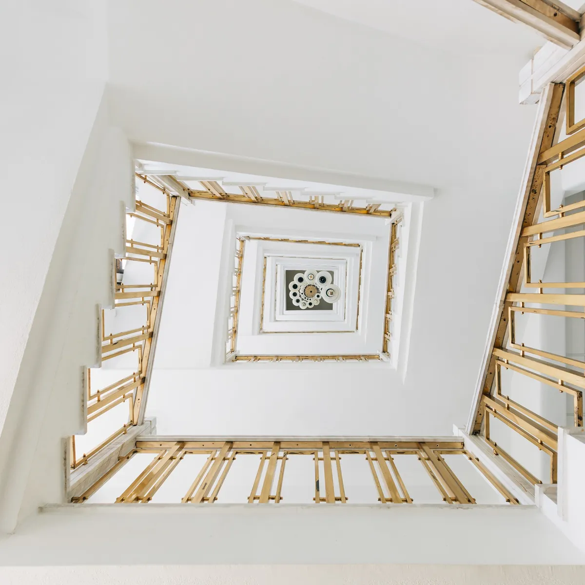 Blick von unten in ein weißes Treppenhaus mit goldenen Geländern.